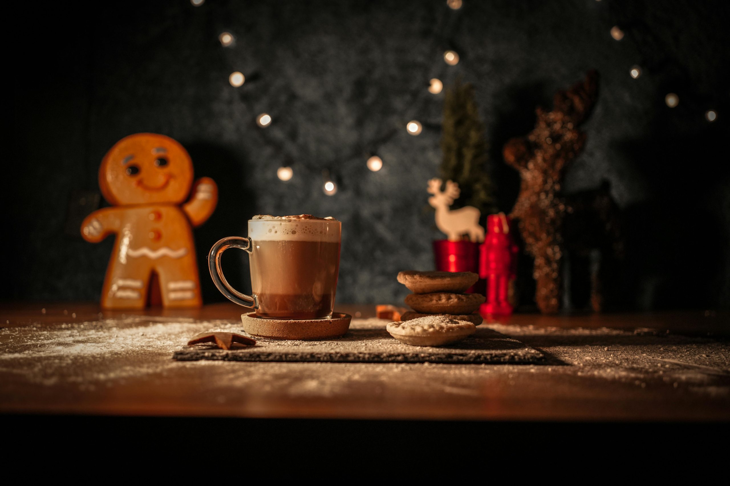 Warm Christmas scene featuring hot chocolate, mince pies, and a gingerbread man with festive lights.