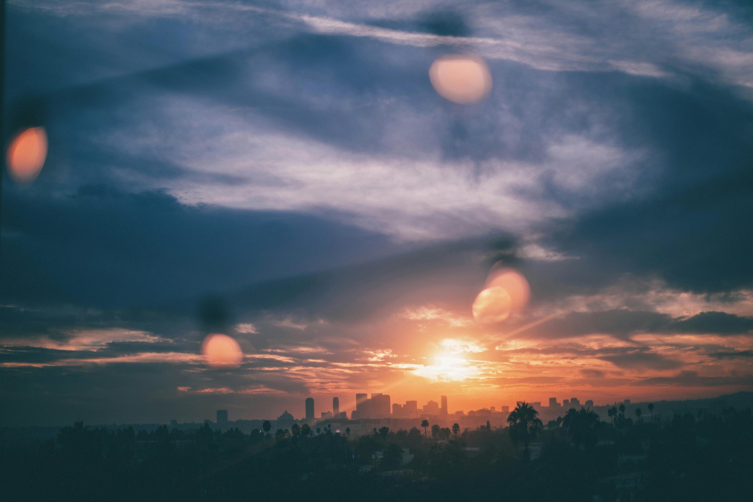 Dramatic sunset view of Los Angeles skyline with fairy lights and cloudy skies.
