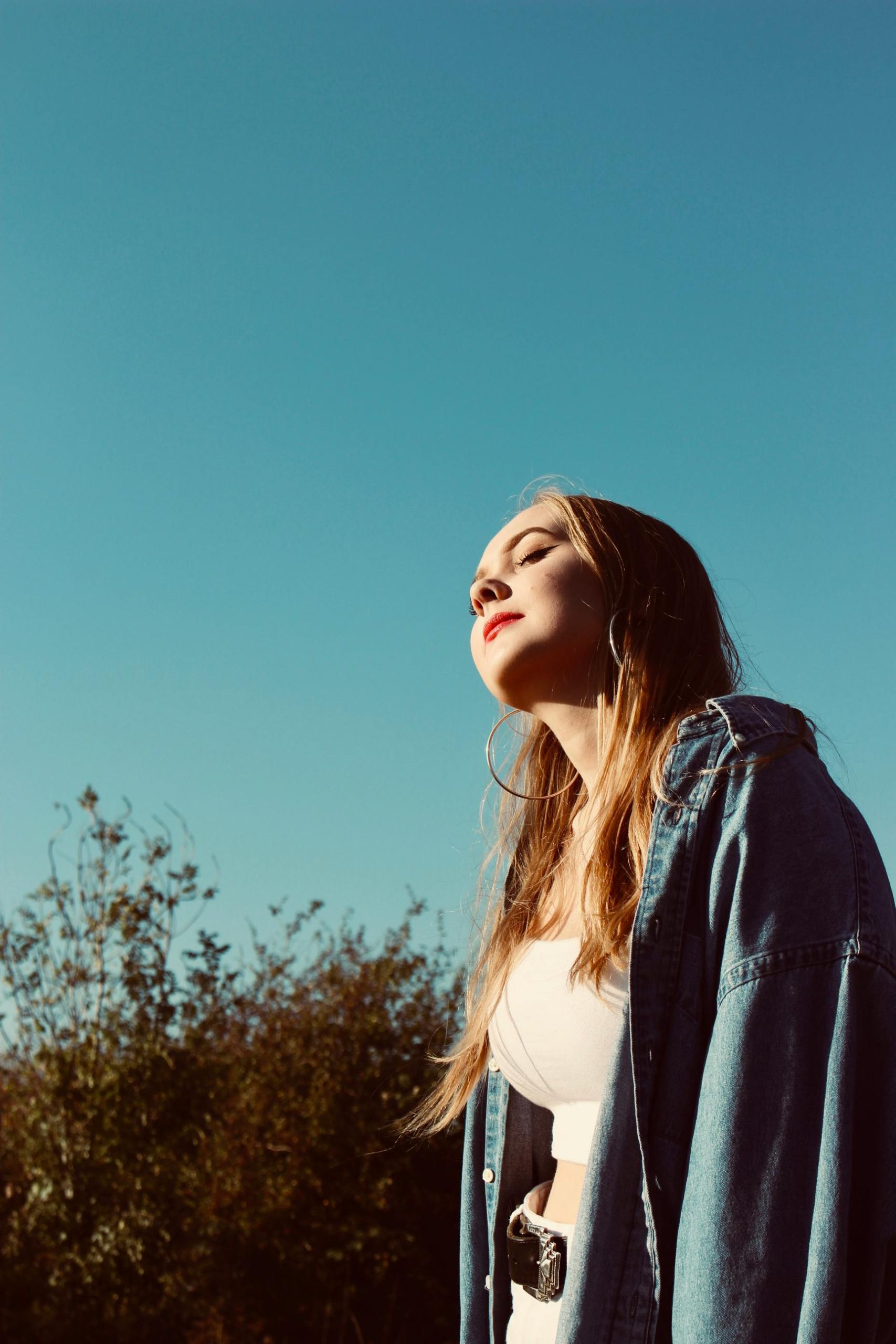 A young woman in a denim jacket enjoying sunlight outdoors in rural England.