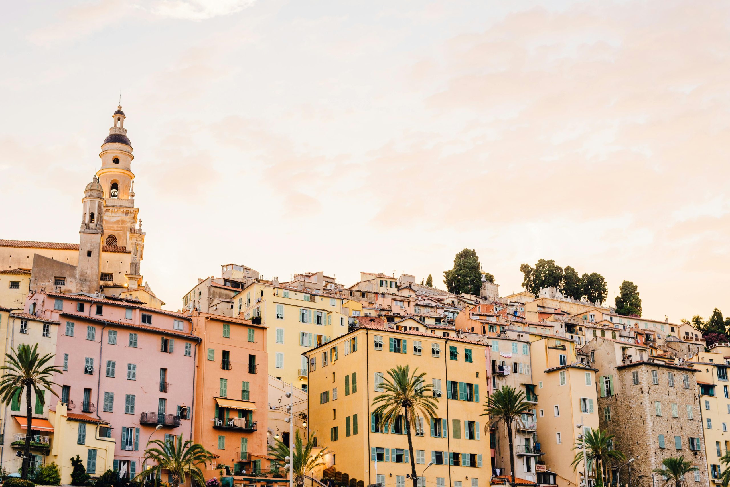 Bright, pastel houses and a historic church in Menton, France, at sunset.