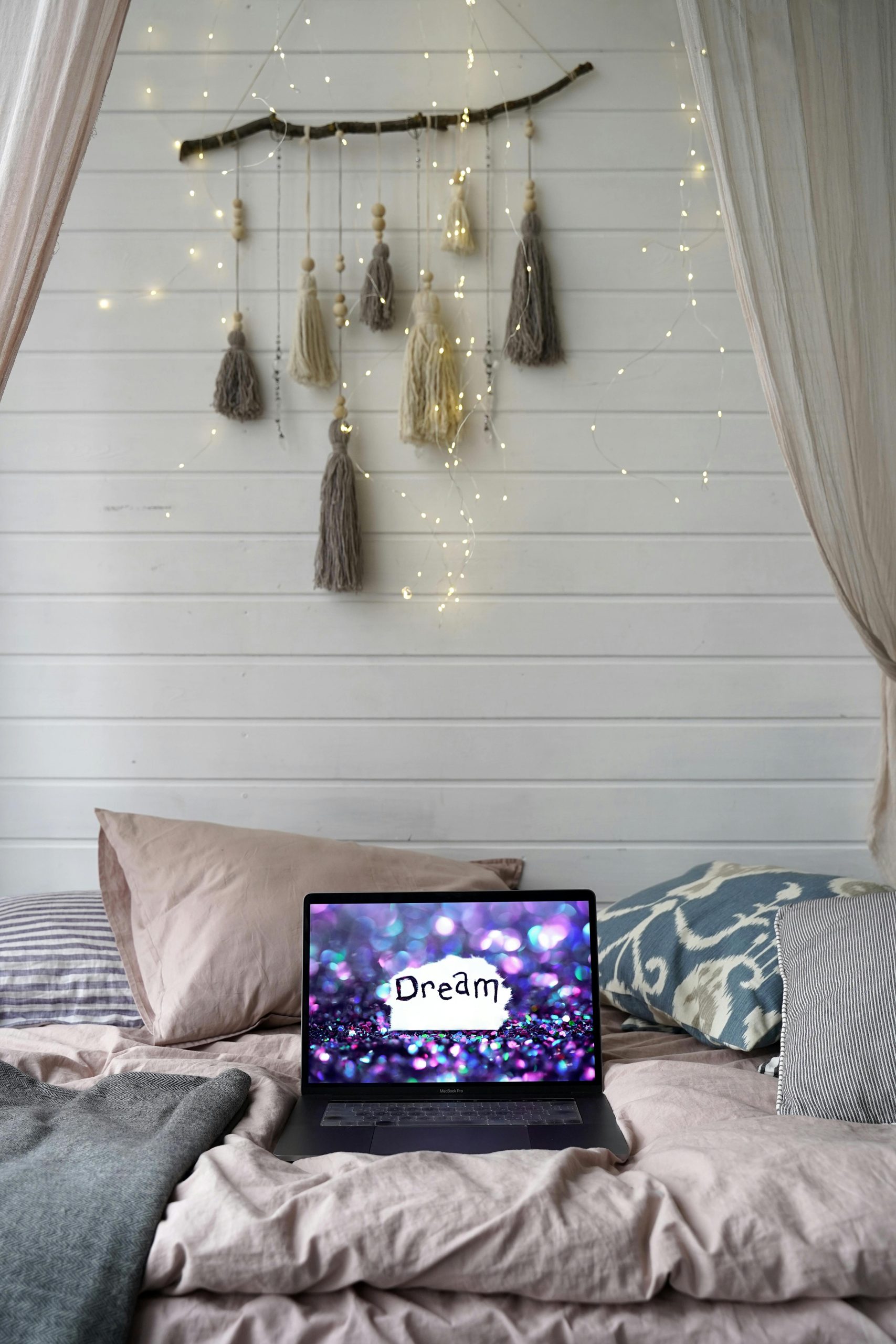 Serene bedroom interior with a laptop displaying 'Dream', decorated with soft pillows and warm lights.