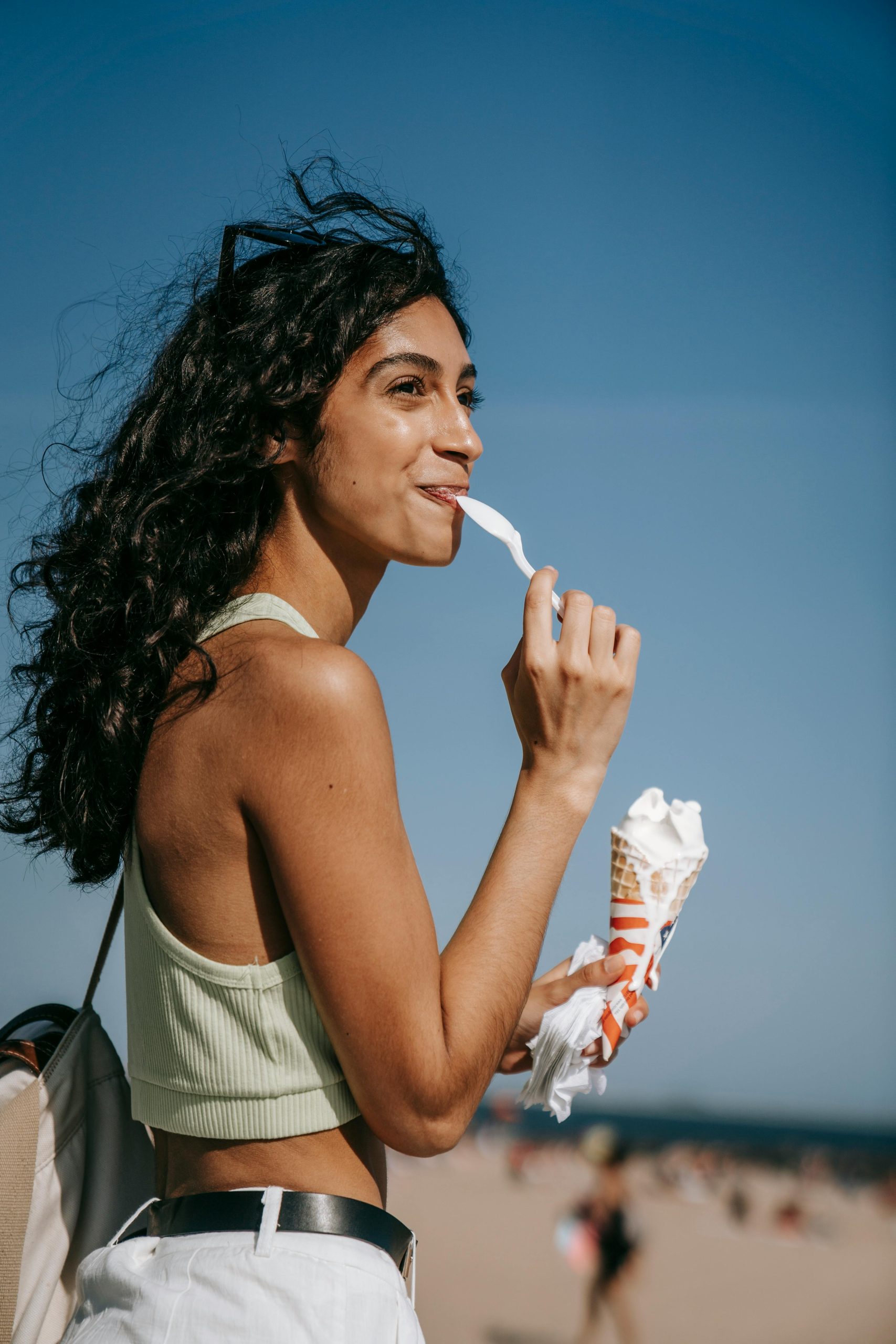 Young woman savoring a vanilla ice cream cone at the beach during summer, embodying leisure and fun.