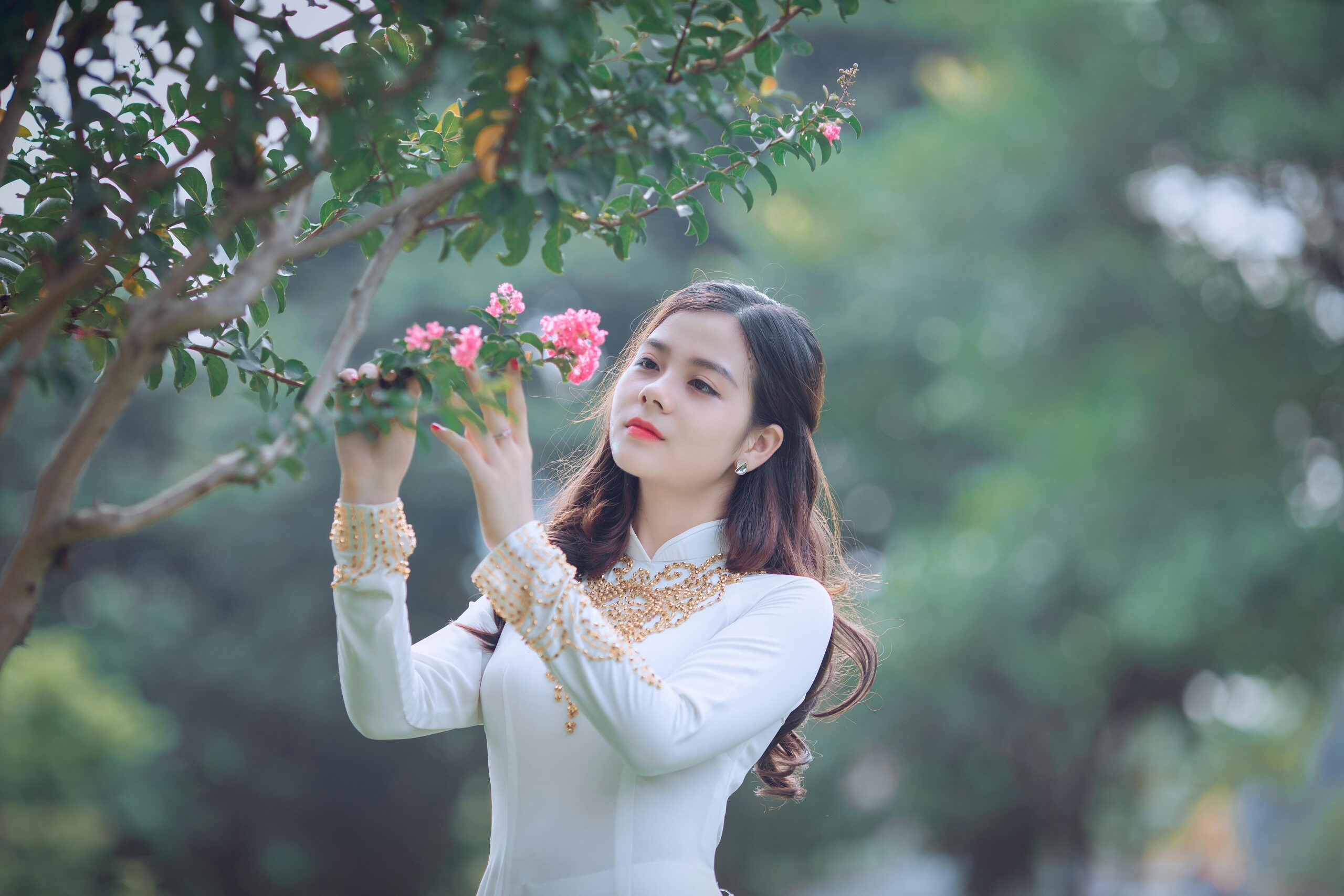 An elegant woman in traditional Ao Dai appreciating the beauty of pink blossoms.