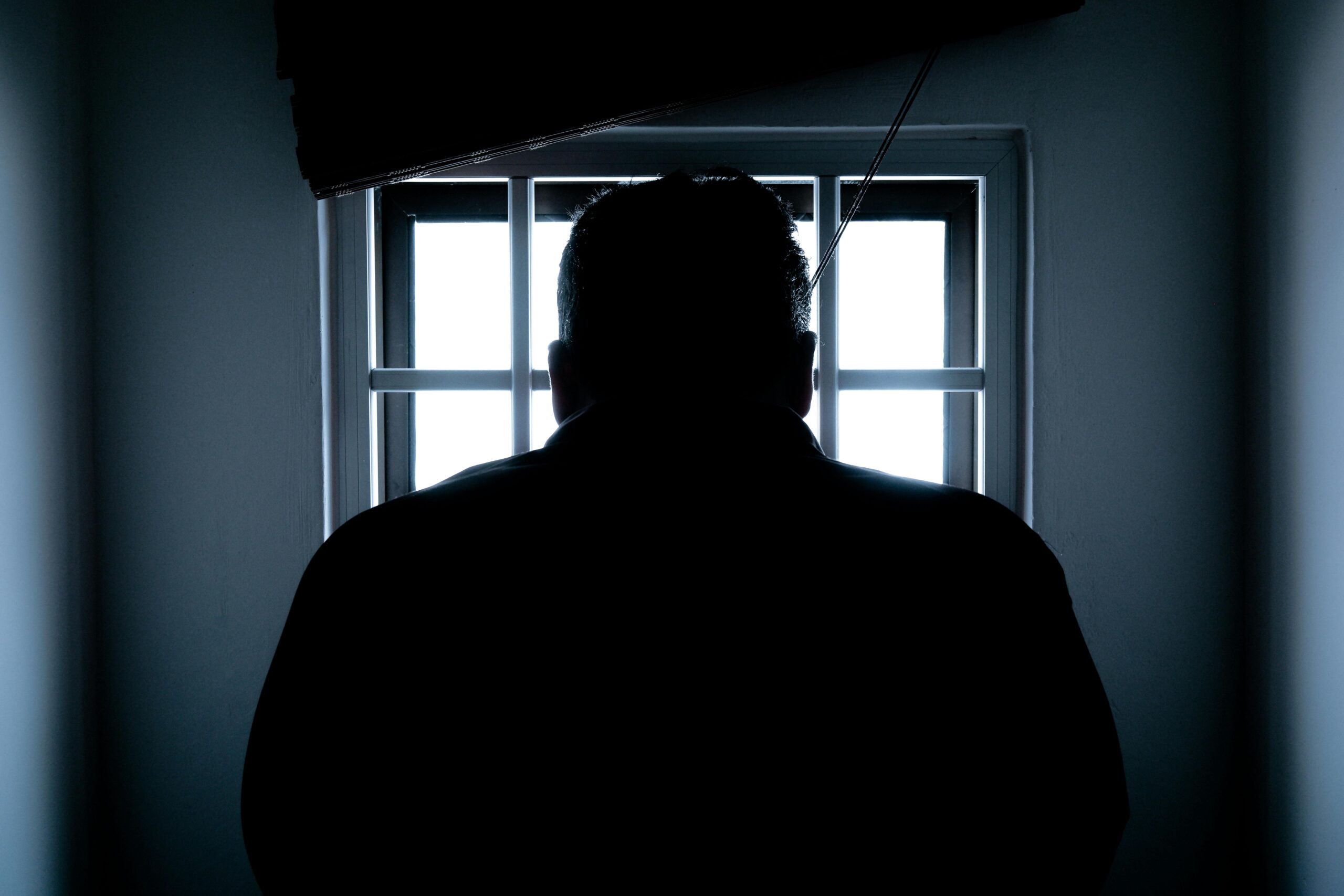Dark silhouette of a man in a prison cell, backlit by window bars.