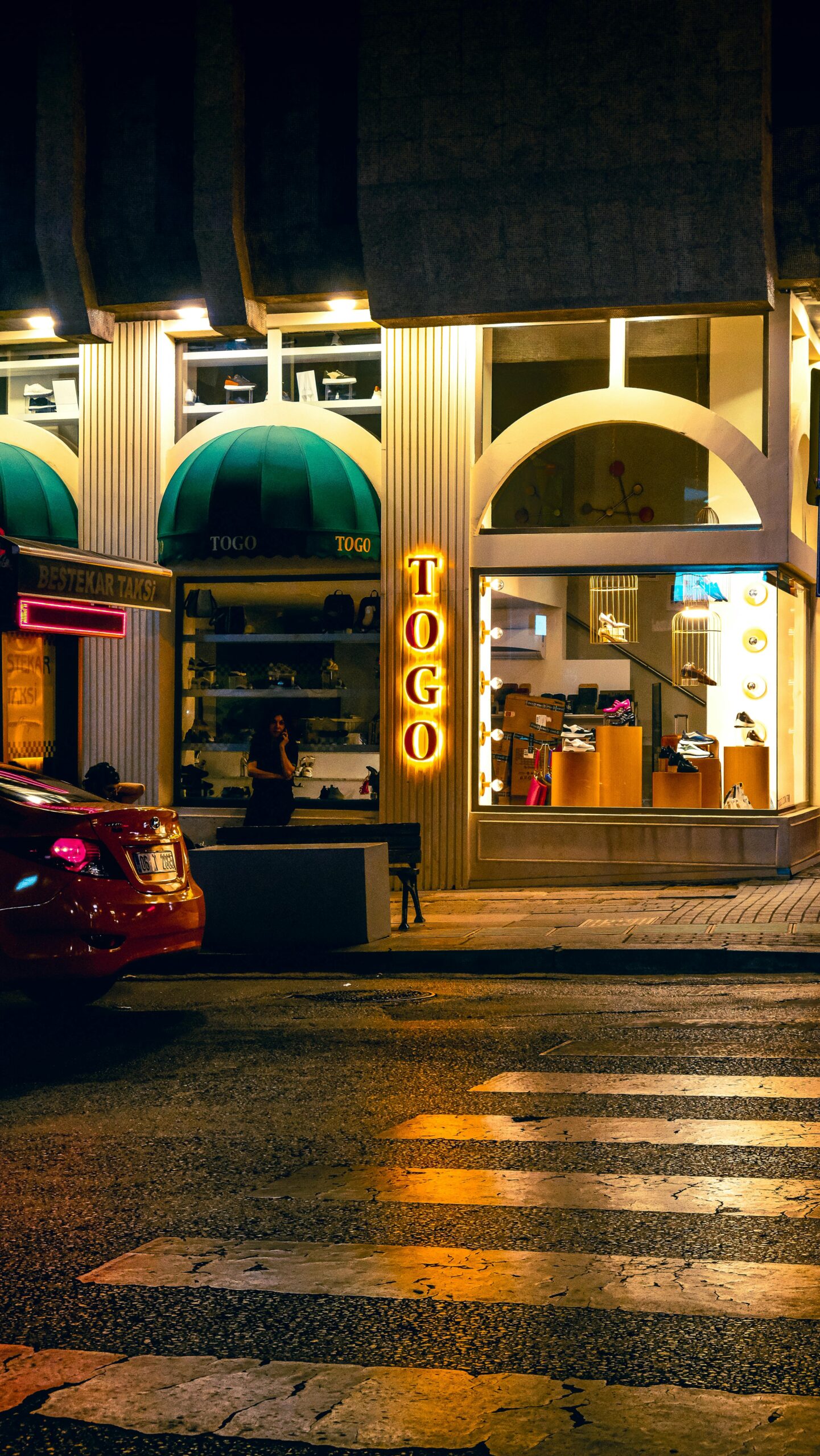 Street view of an illuminated boutique with 'TOGO' sign at night, capturing urban nightlife ambiance.