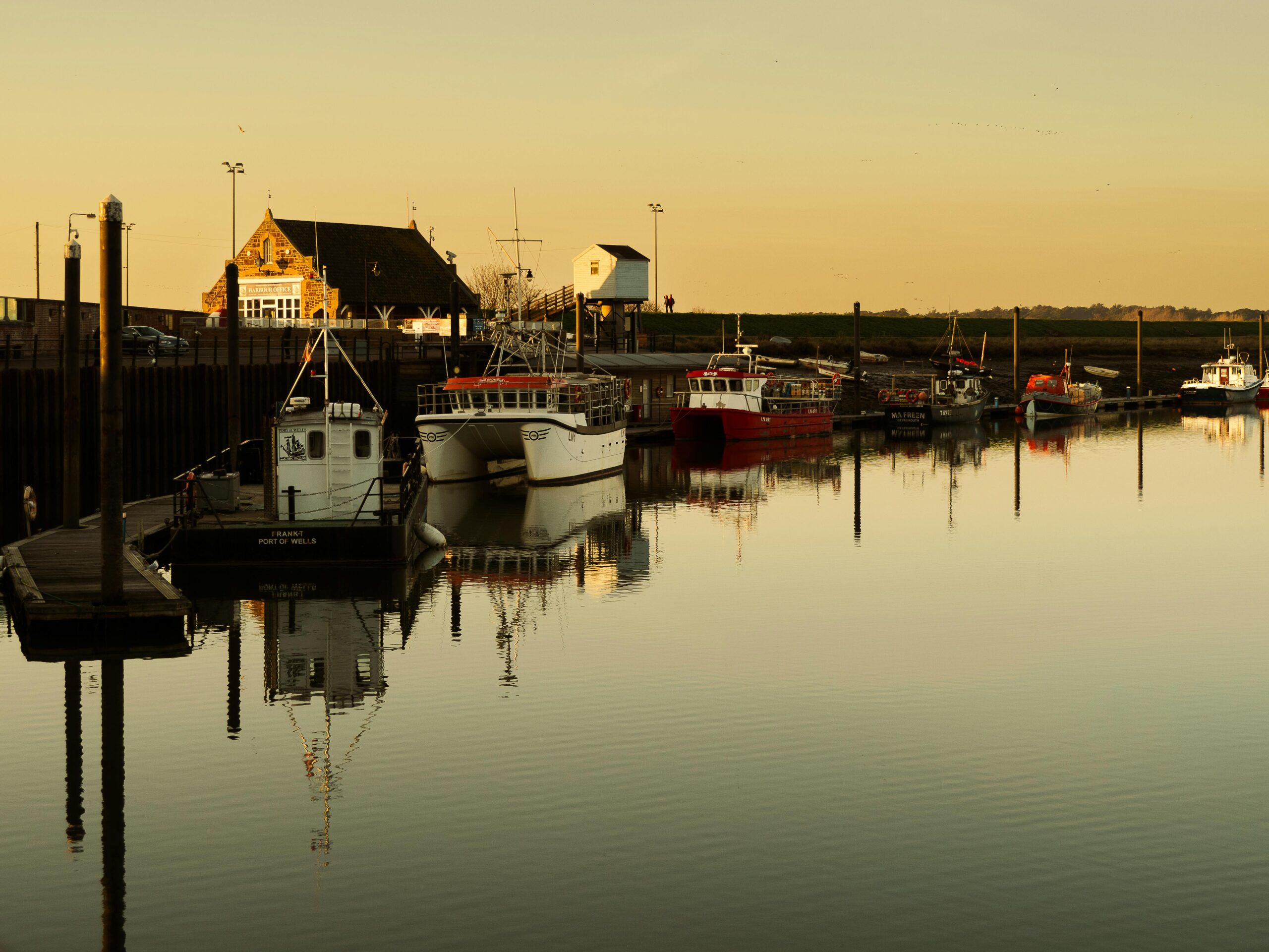 Calm waters and fishing boats at sunset in Wells-next-the-Sea harbor, England.