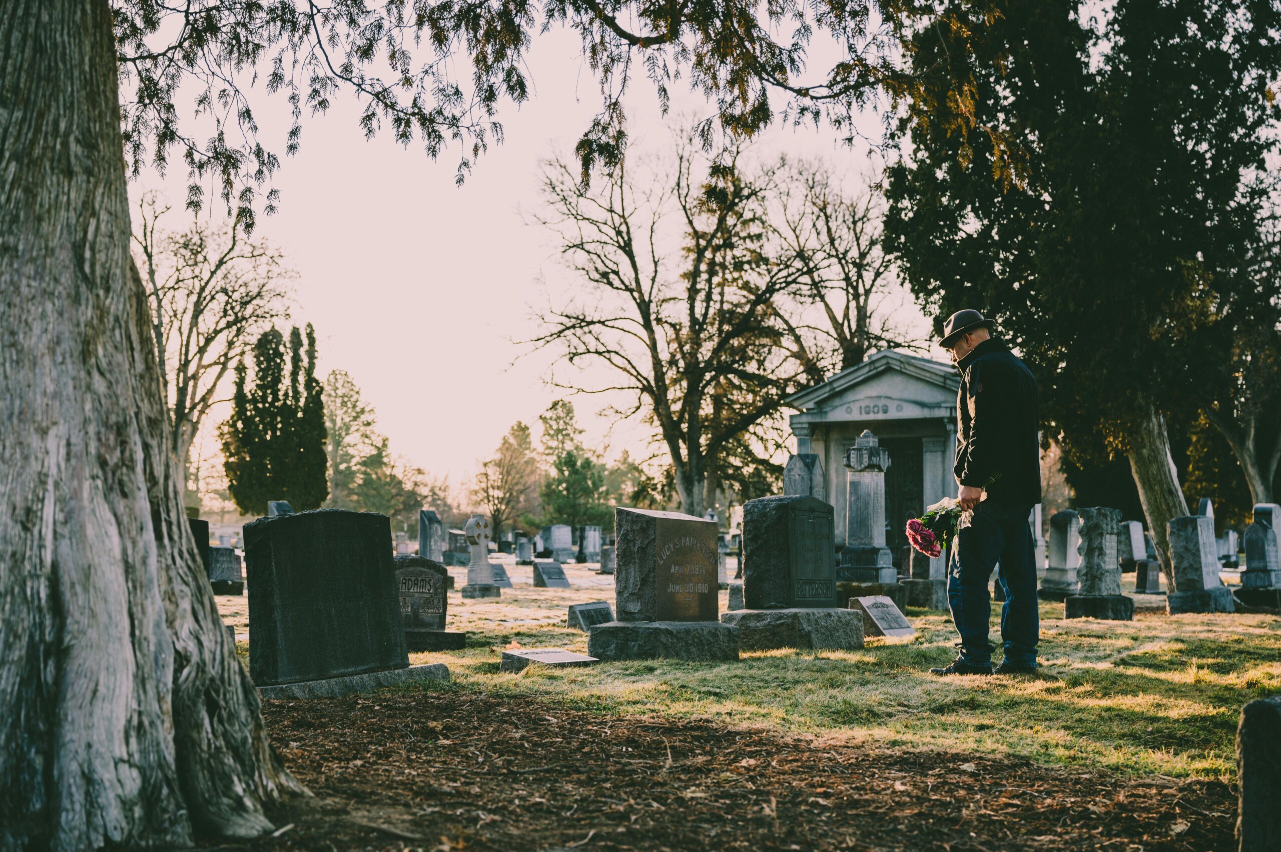 A person stands in a peaceful cemetery holding flowers in remembrance.