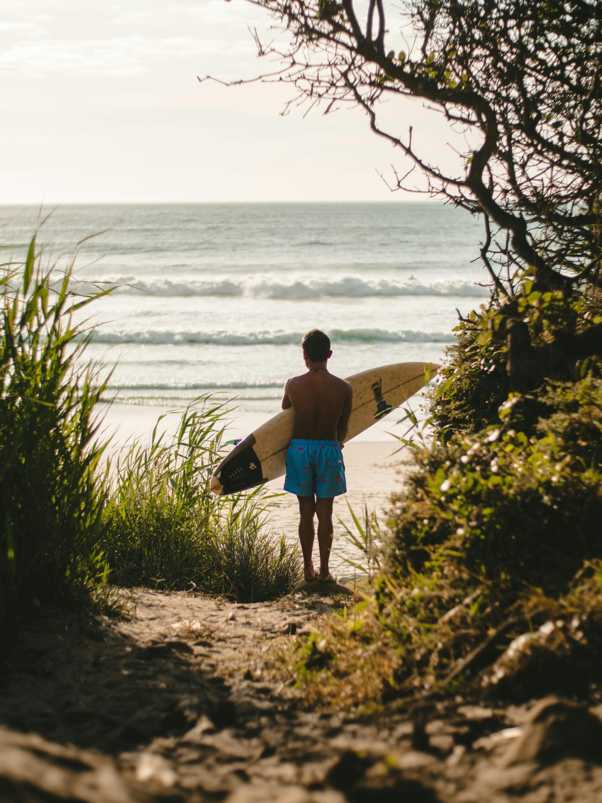 Vivre de sa passion : mythe motivant ou stratégie lucide ? 2 A young boy holds a surfboard while standing on a tropical beach at sunset