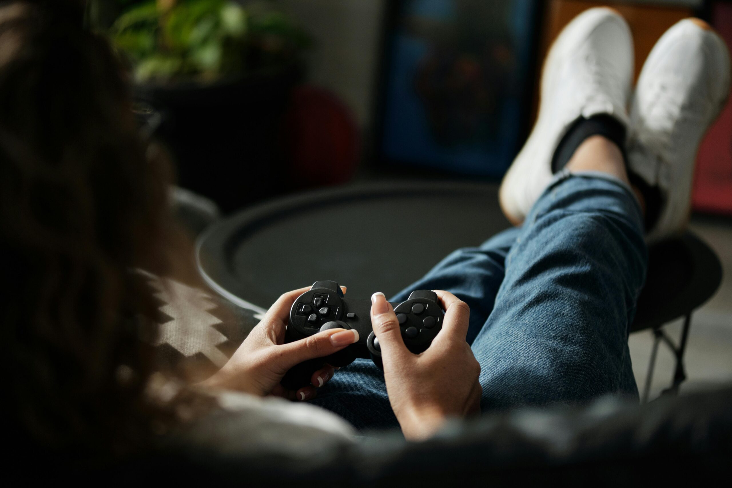 Close-up of woman gaming with a controller, feet propped up, enjoying leisure time indoors.