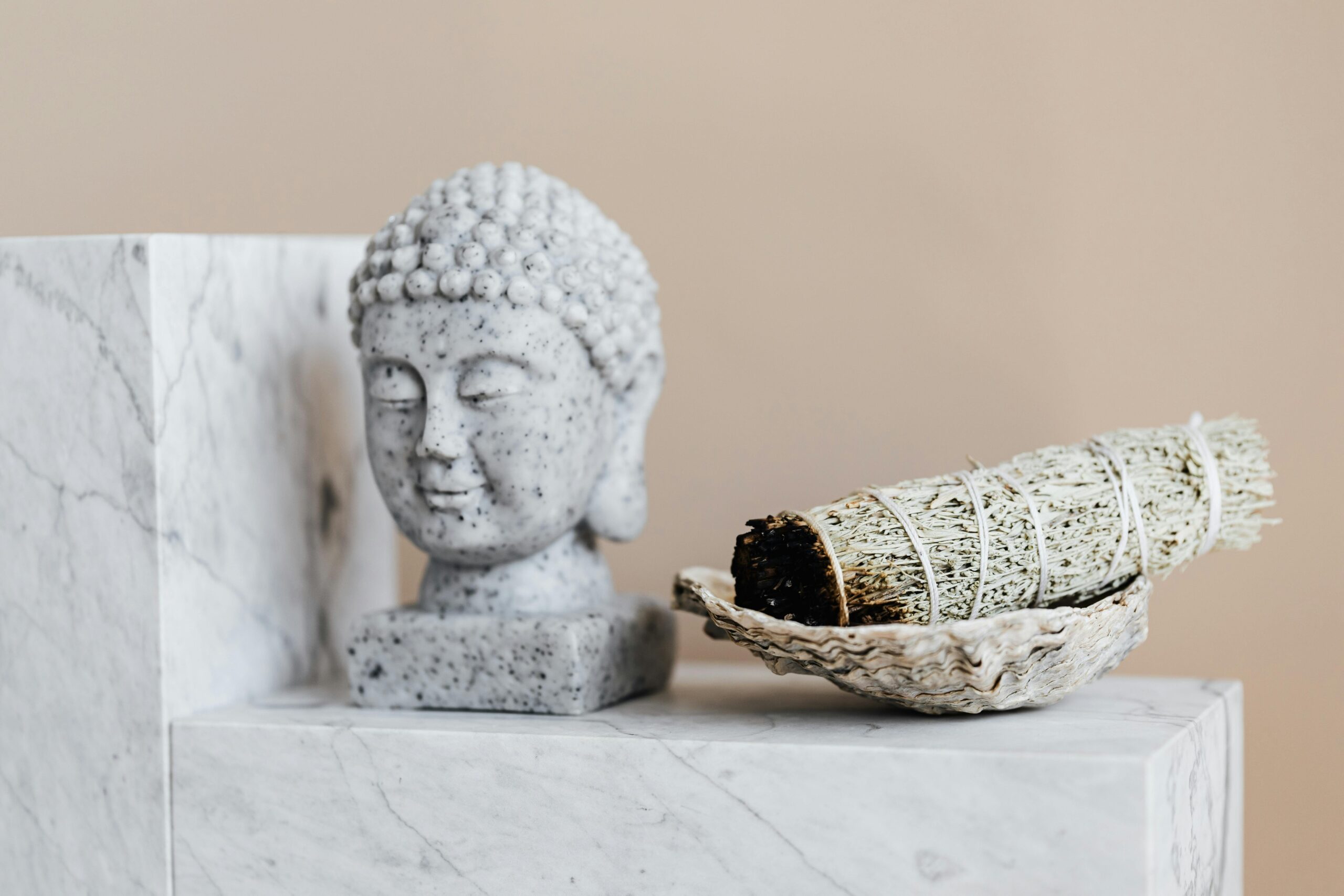 A serene Buddha sculpture with a sage bundle on a marble background, perfect for meditation spaces.