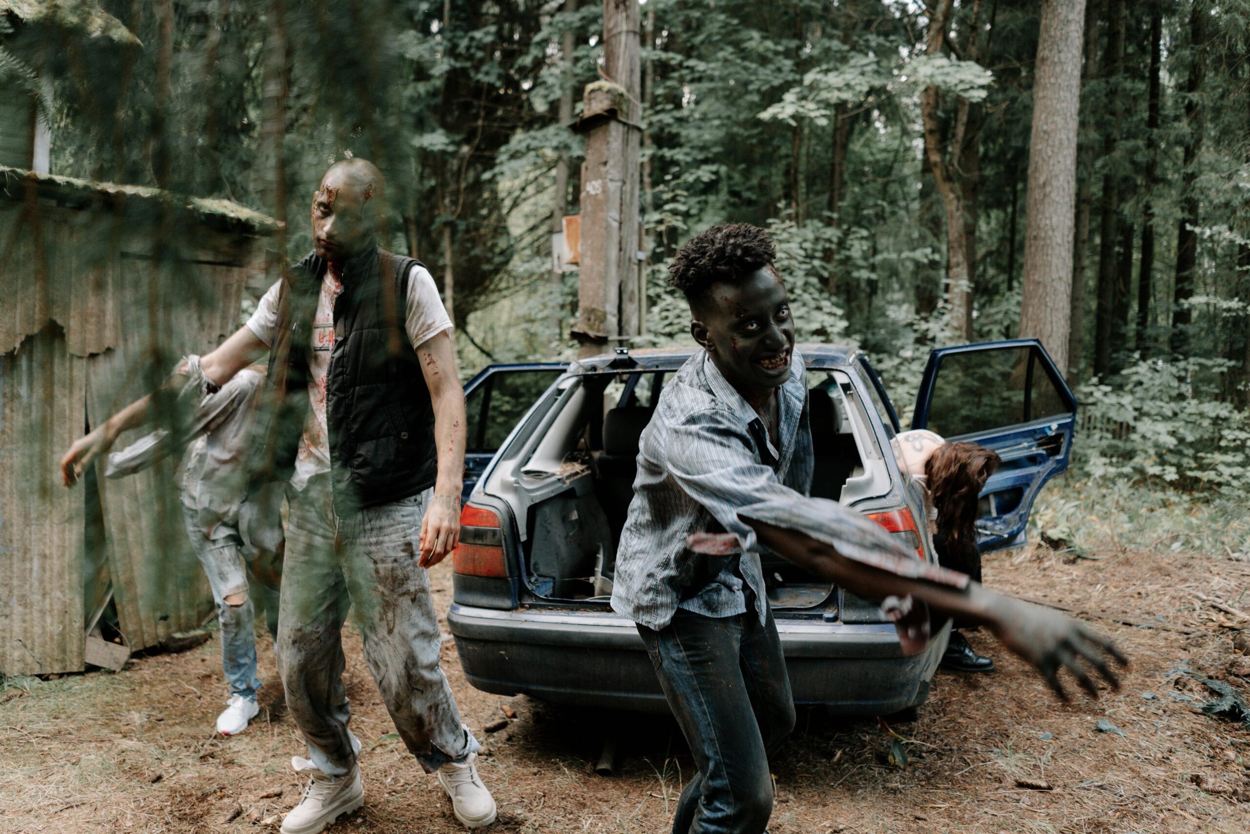 A group of zombies walking near an abandoned car in a creepy forest setting.