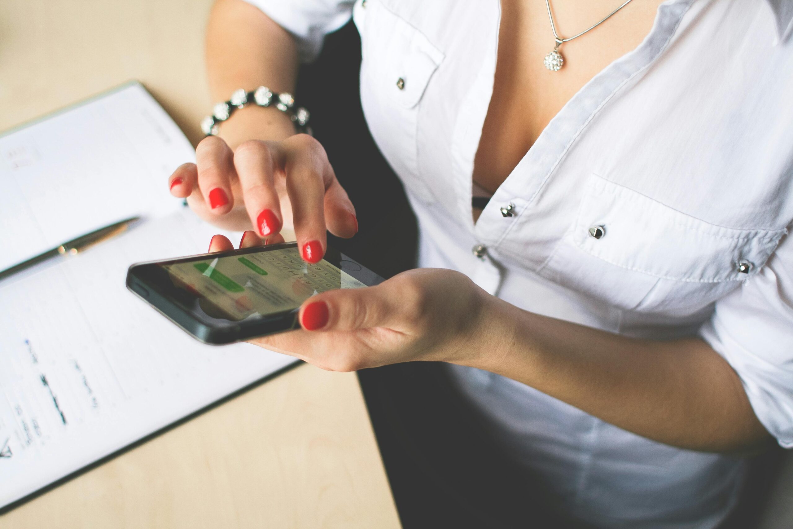 Close-up of a woman with red nail polish using a smartphone indoors, showcasing technology and lifestyle.