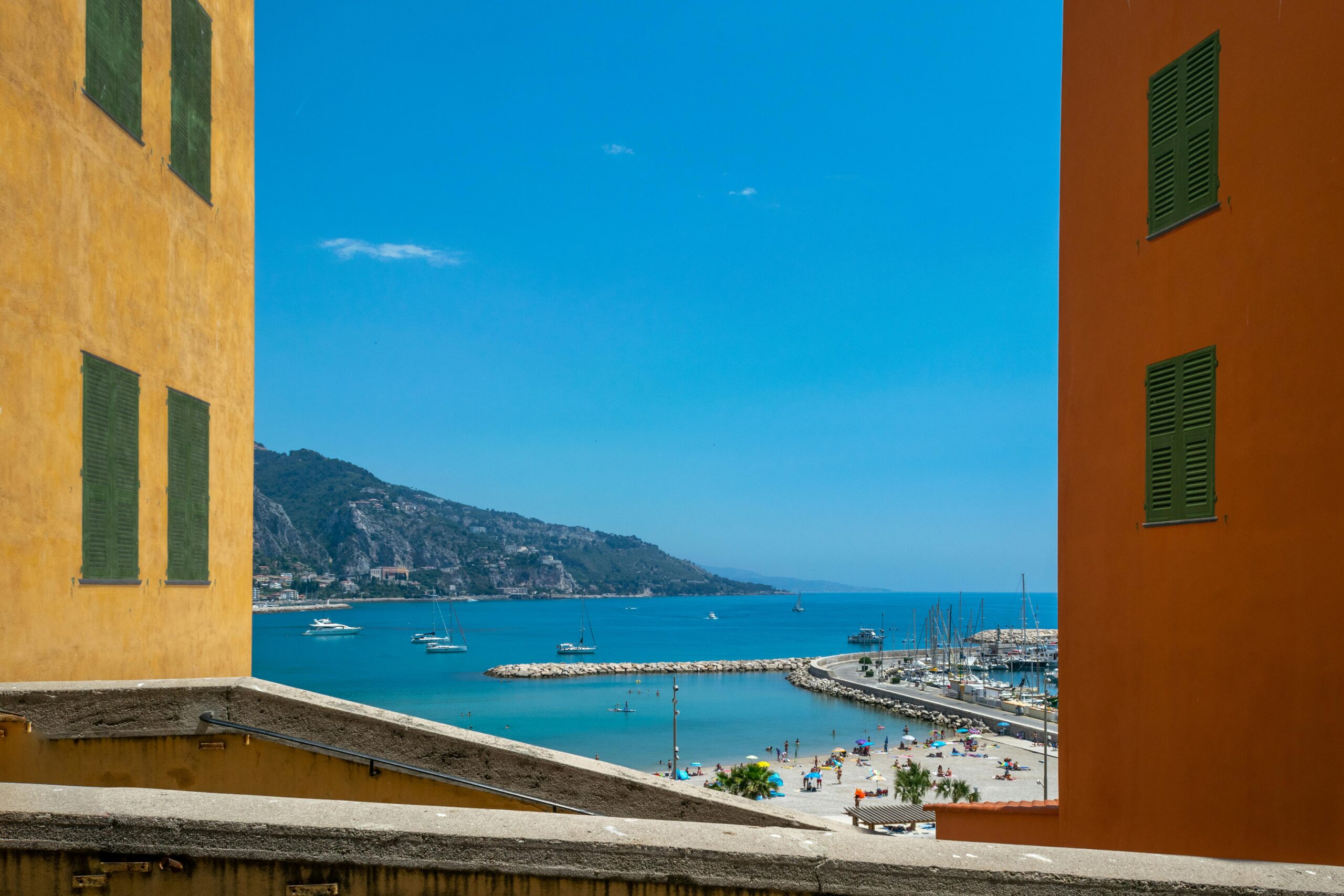 Vibrant cityscape of Menton with a stunning beach and marina view framed by colorful buildings.