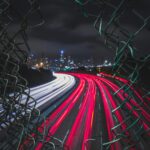 Long exposure captures urban expressway lights through a broken fence at night in San Francisco.