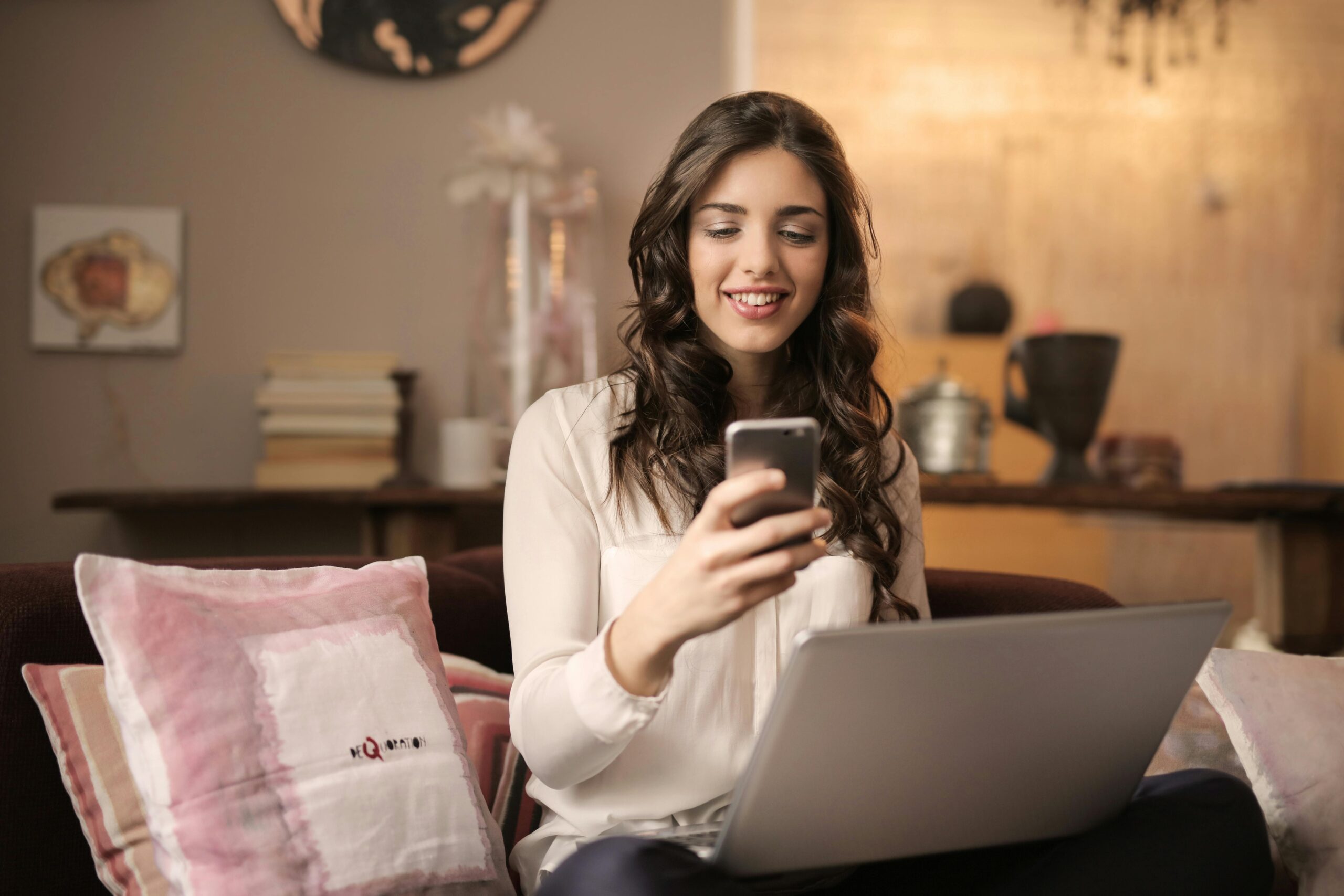 Créer un business en ligne pour générer des revenus 2 A woman enjoying leisure time using her smartphone and laptop in a cozy living room.