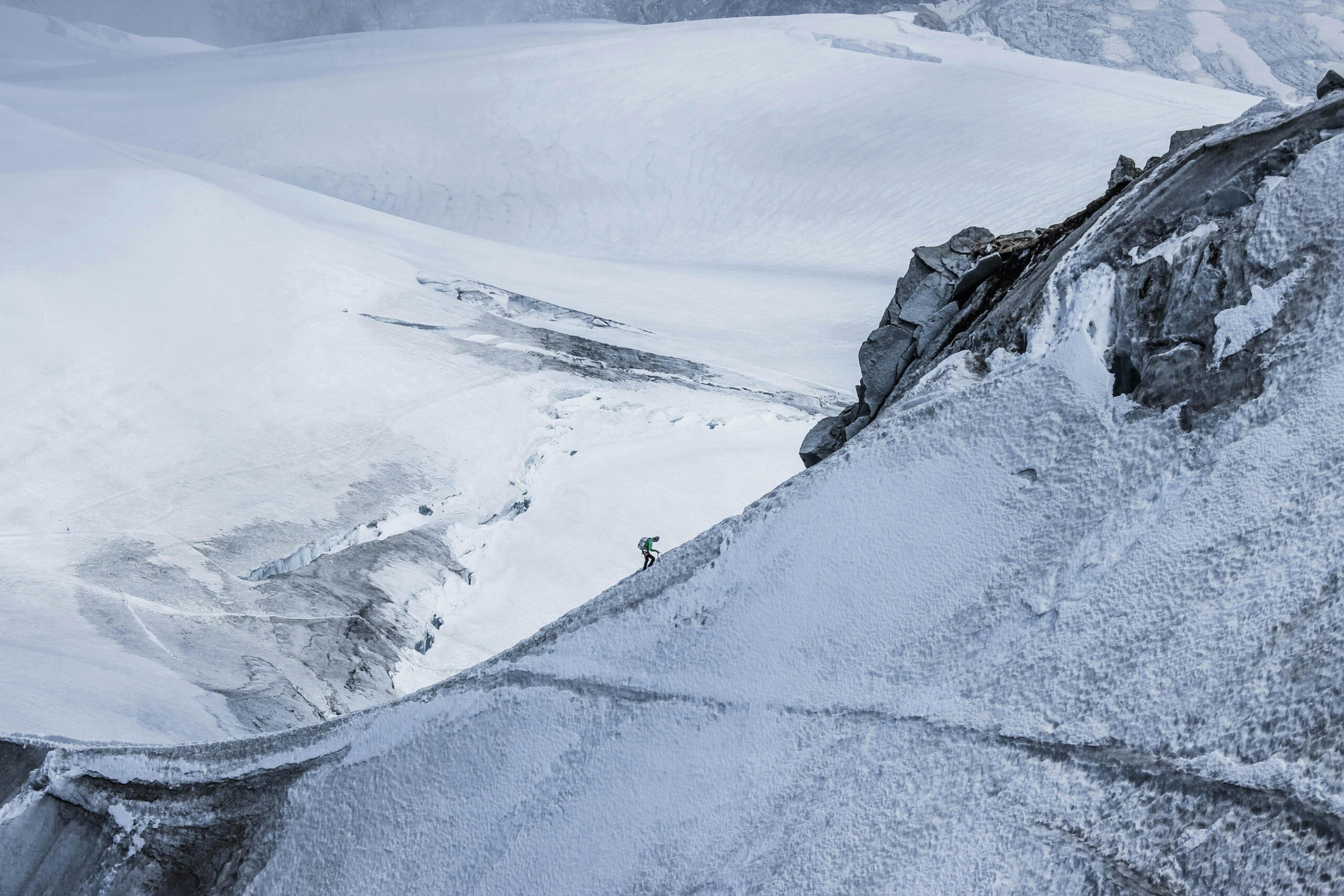 From above distant alpinist on snowy rough mountain slope against frozen spacious mountainous valley in daylight