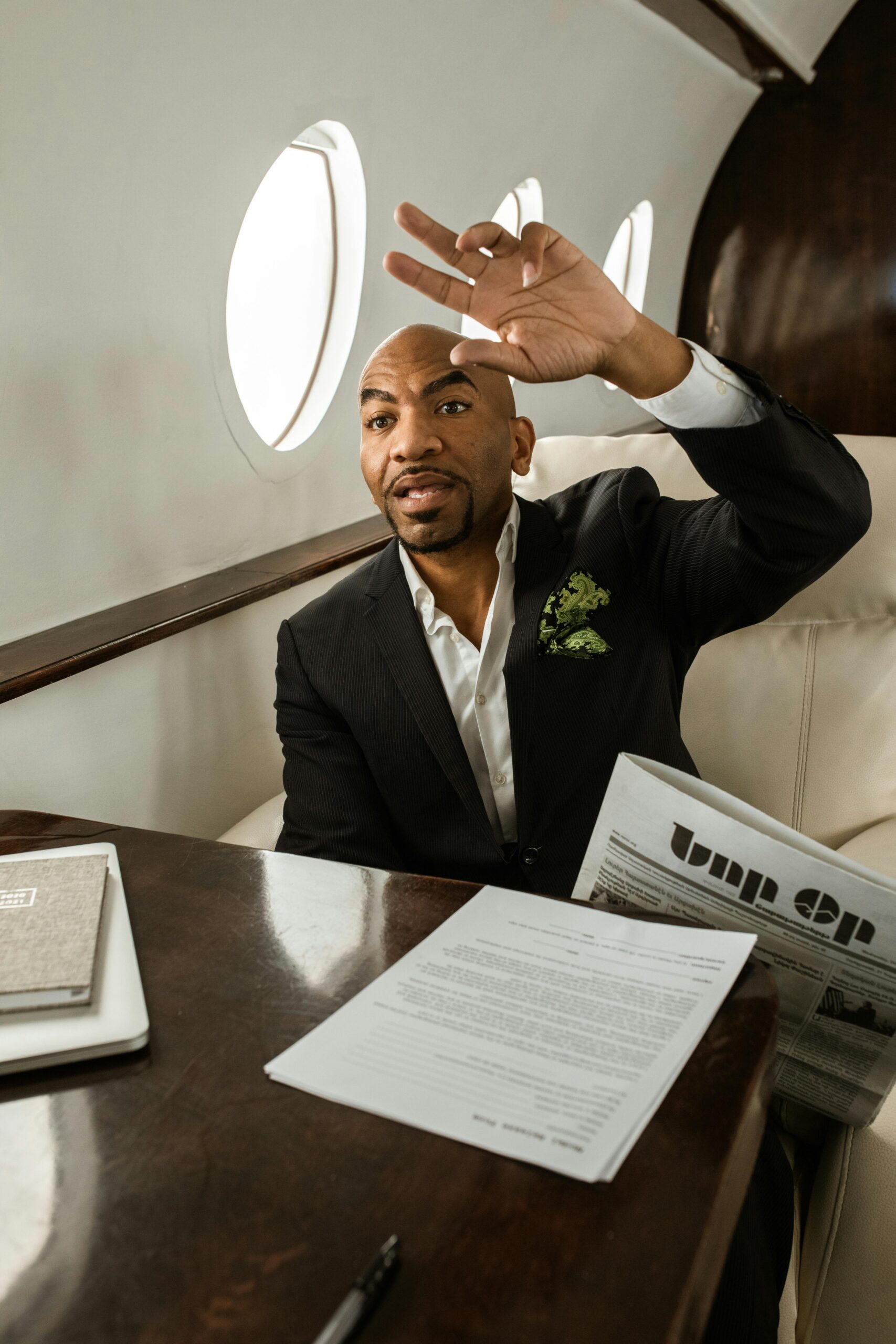 Elegant businessman sitting in a private jet cabin, reading a newspaper and making a gesture.