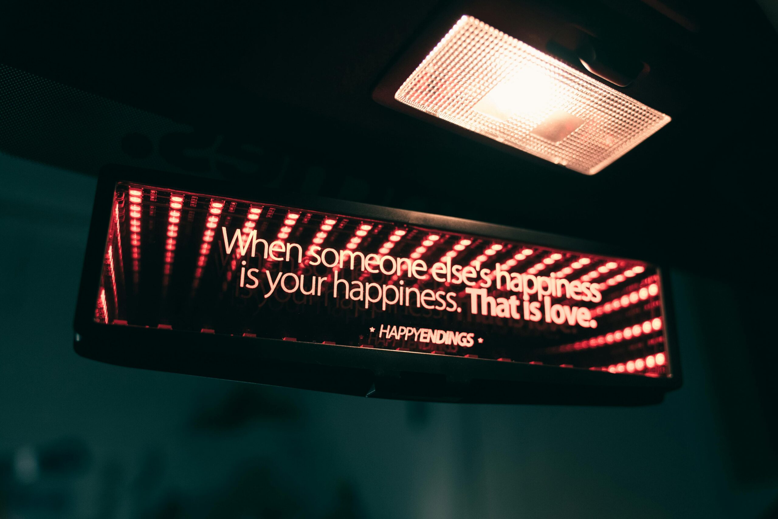 Rearview mirror with an inspirational quote about love and happiness, illuminated in a dim car interior.