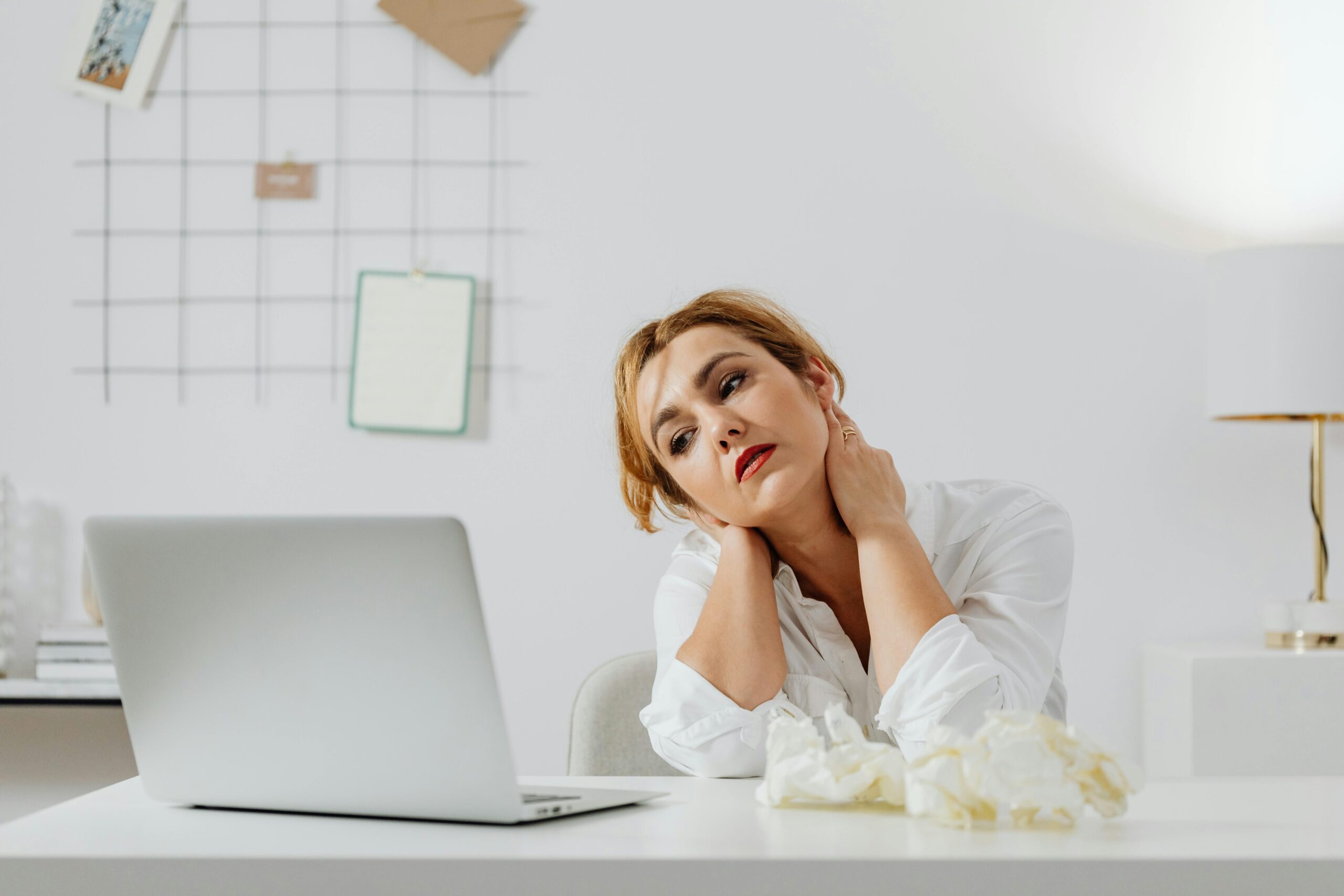 Tired woman sitting at desk with a laptop, appearing weary in a modern workspace.