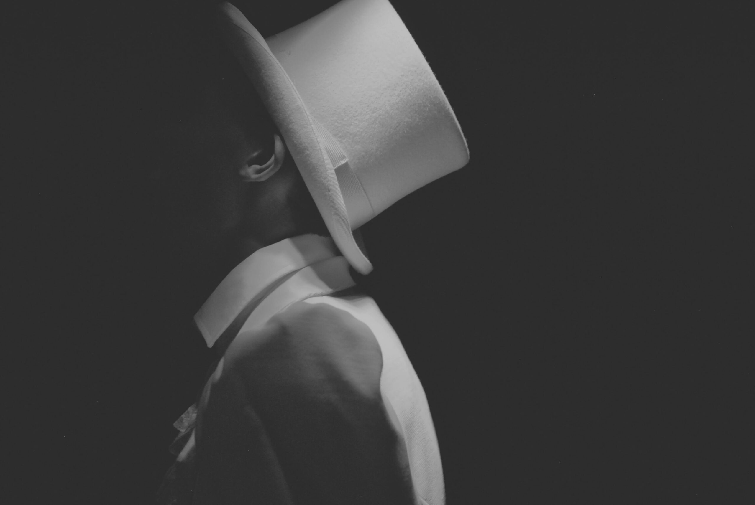 Confiance en soi jalousie : 7 vérités puissantes pour transformer l’insécurité en force 3 Dramatic black and white portrait of a man in profile wearing a top hat, surrounded by shadows.