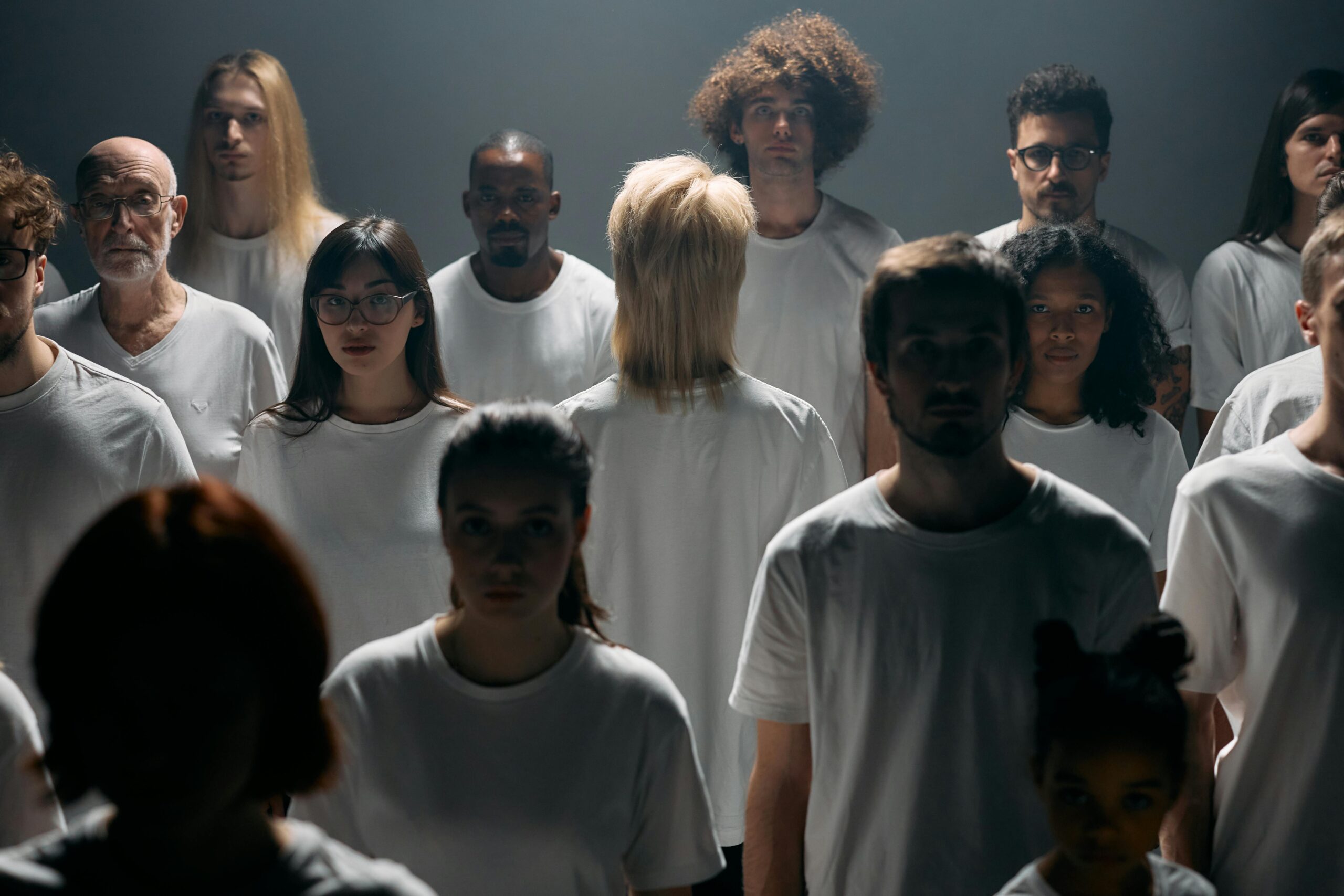 A diverse group of individuals in white shirts standing in a studio setting.