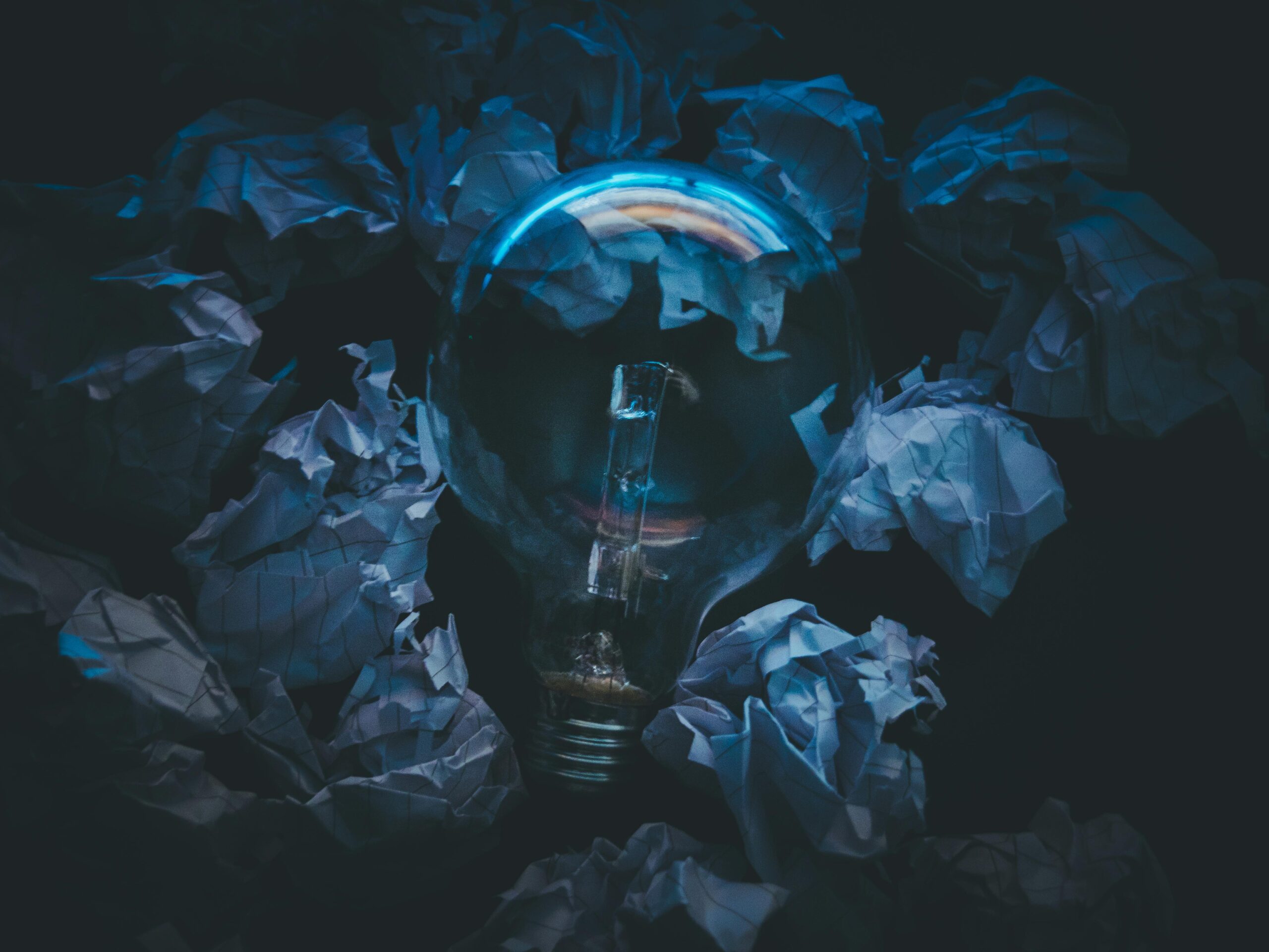 Comment trouver la bonne idée de livre 4 A light bulb surrounded by crumpled paper symbolizes creative ideas and innovation in a dark setting.