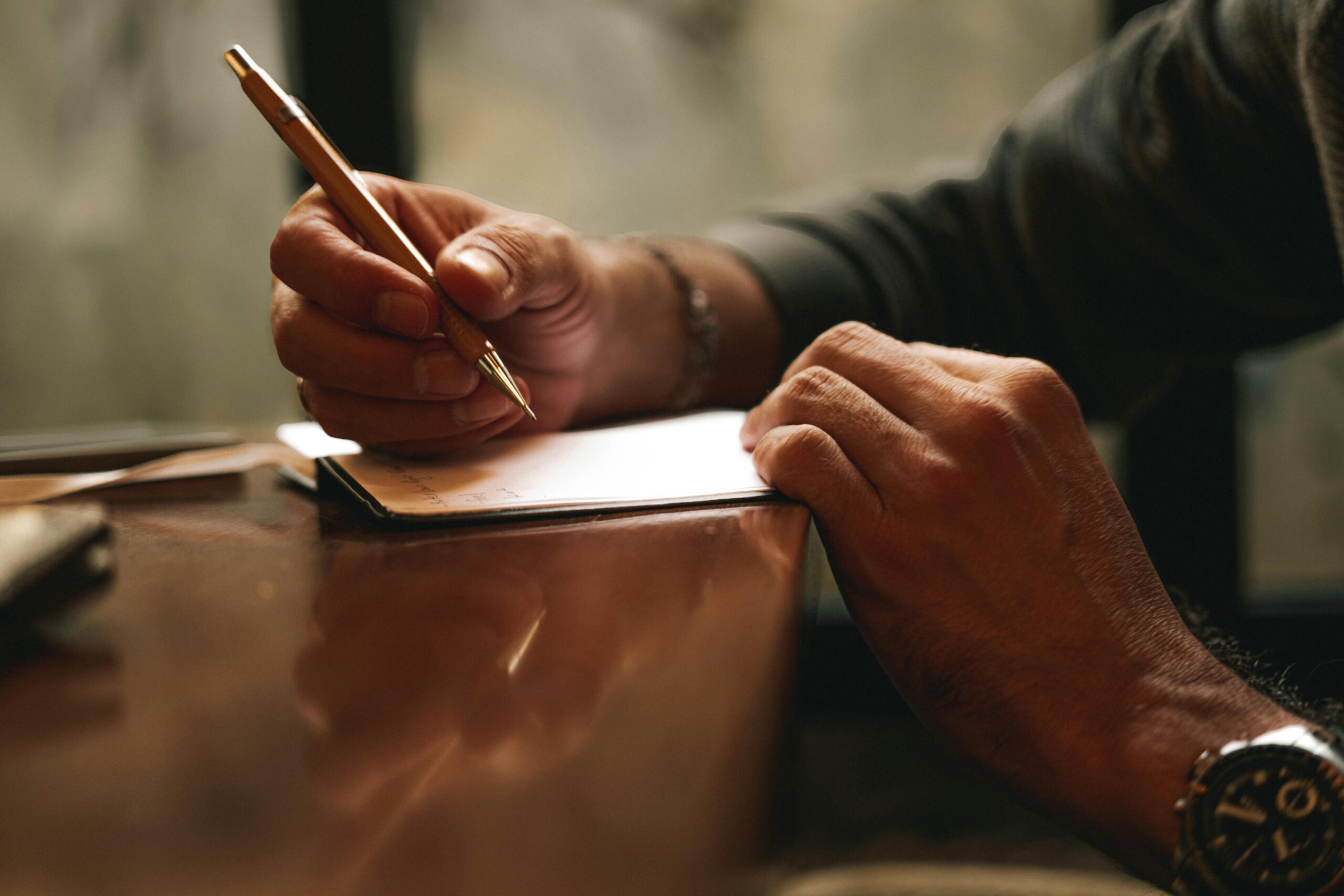 Man writing with a pen on a desk, depicting focus and concentration.