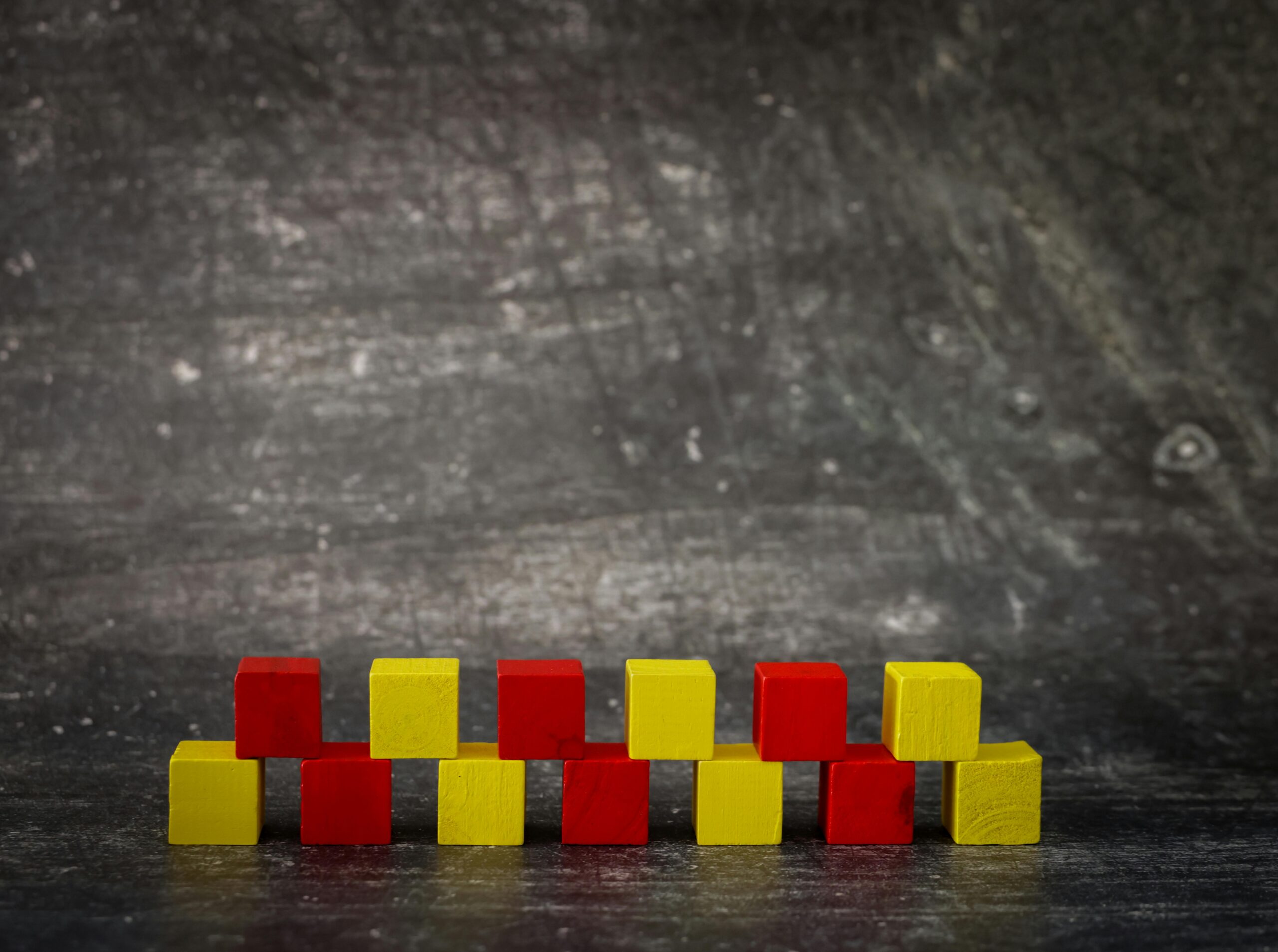 A set of red and yellow wooden blocks neatly arranged against a textured dark background.