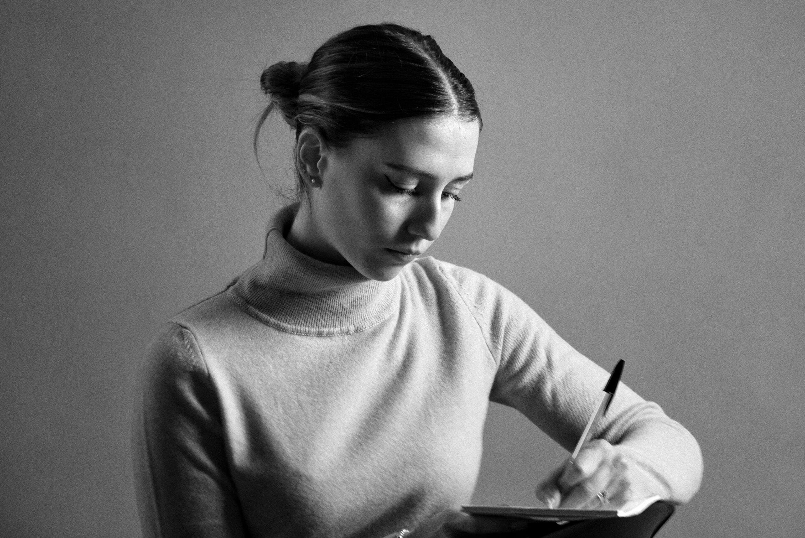 Elegant black and white portrait of a woman writing with focus and concentration.