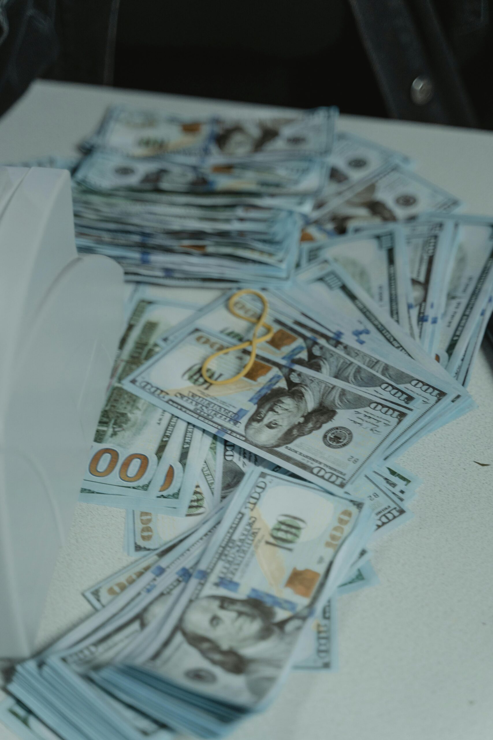 COMMENT ÉCRIRE UN LIVRE SUR L'ARGENT 3 A pile of US dollar bills neatly stacked and secured with a rubber band on a white surface.