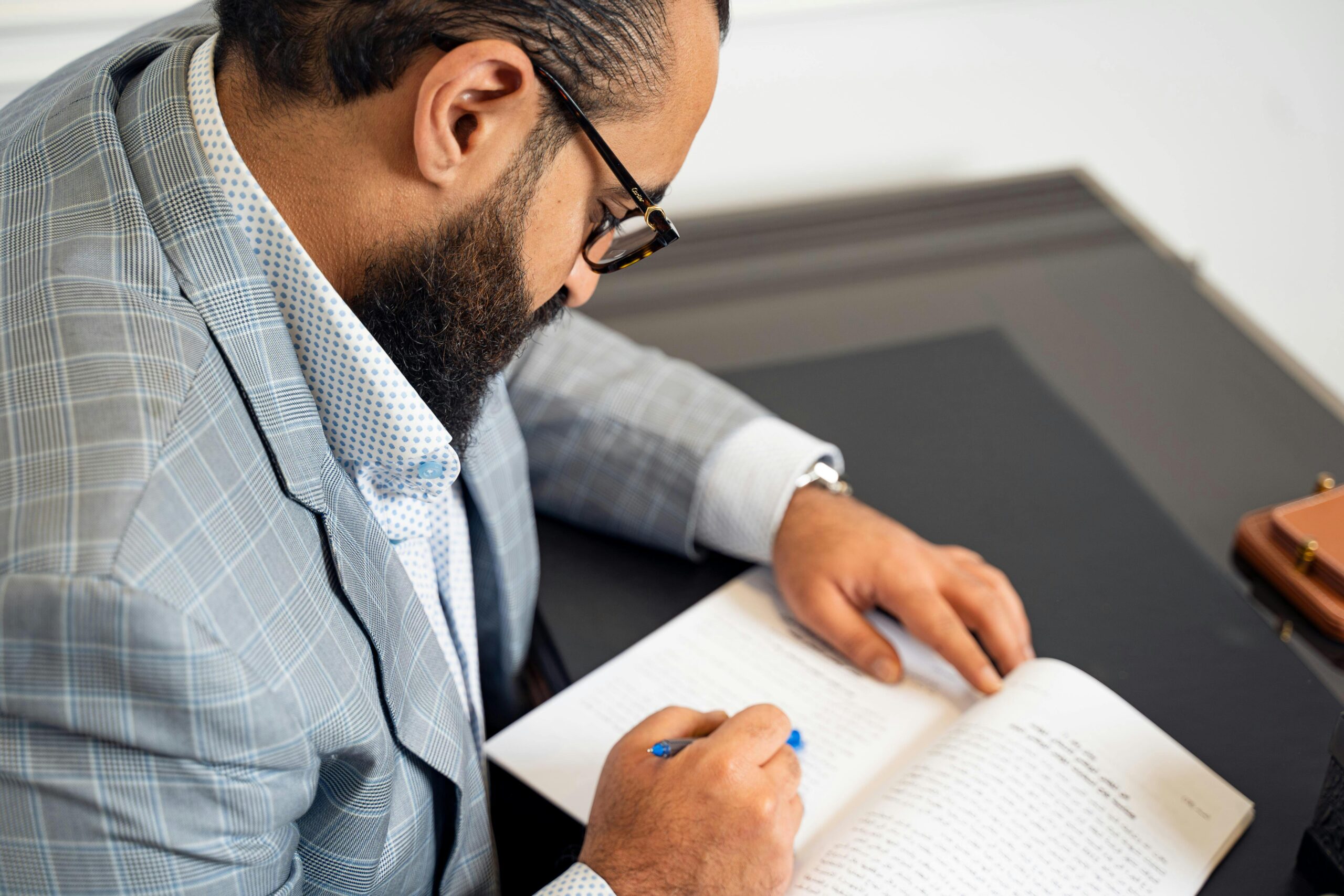 Professional businessman in formal attire writing notes in a notebook at his desk.