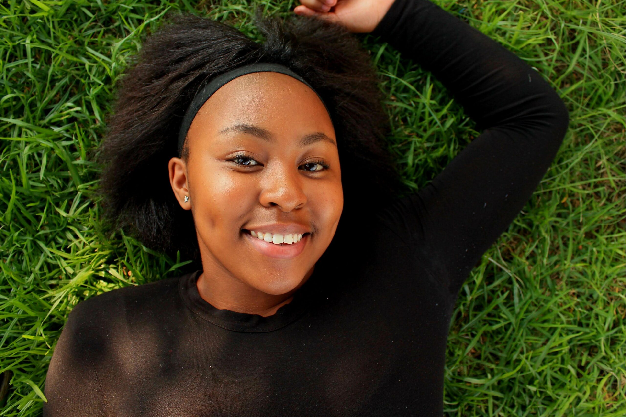 Happy young woman smiling while lying on green grass in a park.