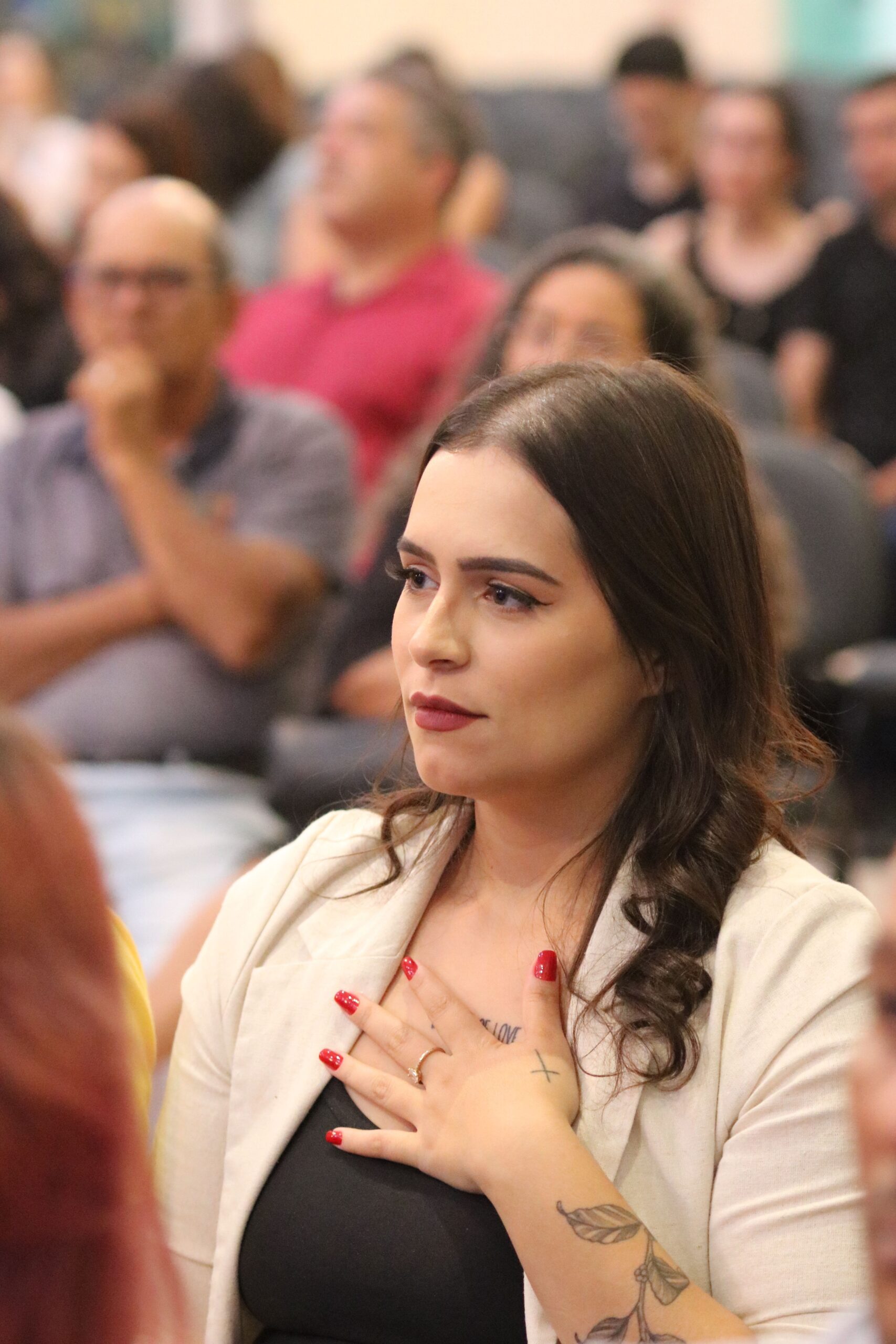 Young woman with tattoos in audience, hand on heart, attentive expression.